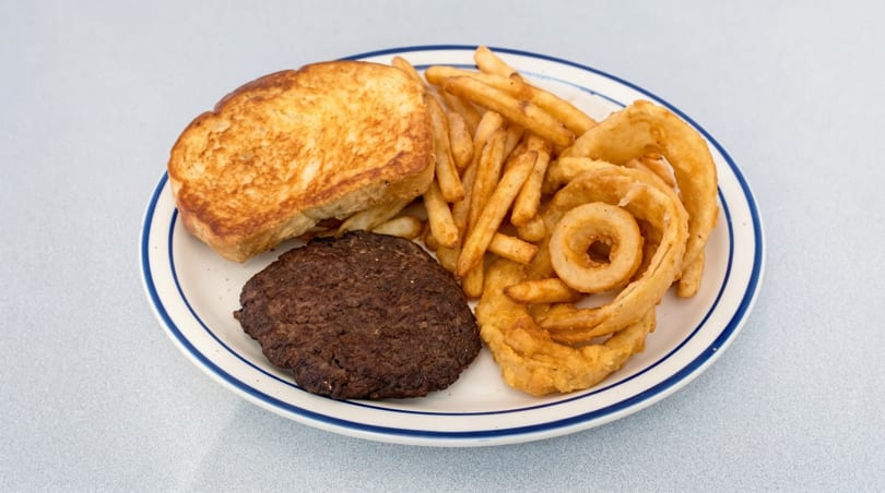 A plate with a hamburger patty, grilled toast, french fries, and onion rings.