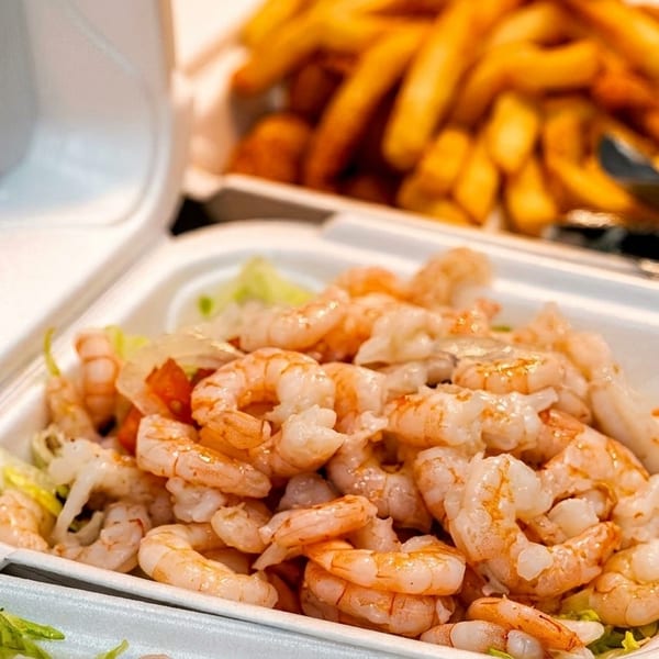 Takeout container filled with shrimp and lettuce, with fries and onion rings blurred in the background.
