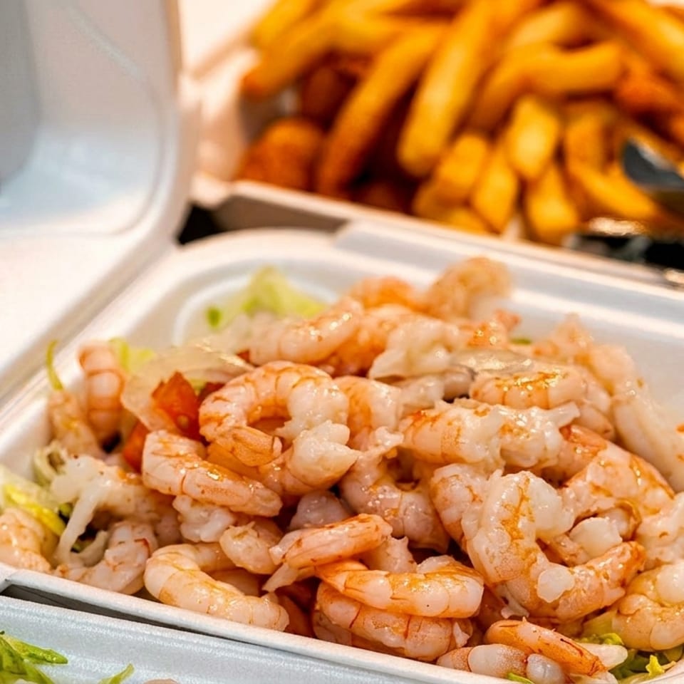 Takeout container filled with shrimp and lettuce, with fries and onion rings blurred in the background.