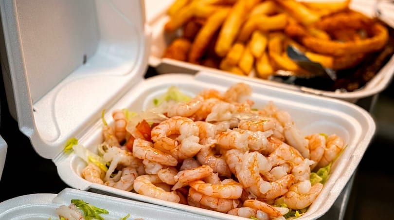 Takeout container filled with shrimp and lettuce, with fries and onion rings blurred in the background.