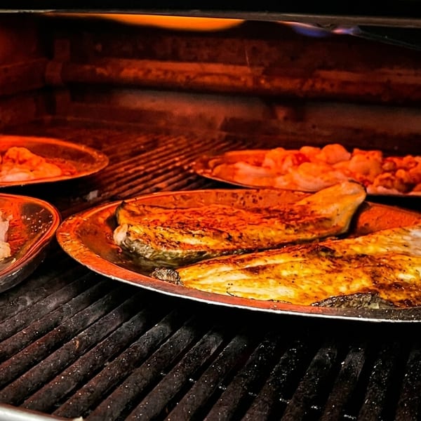 Fish fillets and shrimp cooking on metal trays inside a hot oven with glowing orange light.