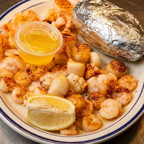 Grilled shrimp and scallops with a lemon wedge, melted butter, and a foil-wrapped baked potato.