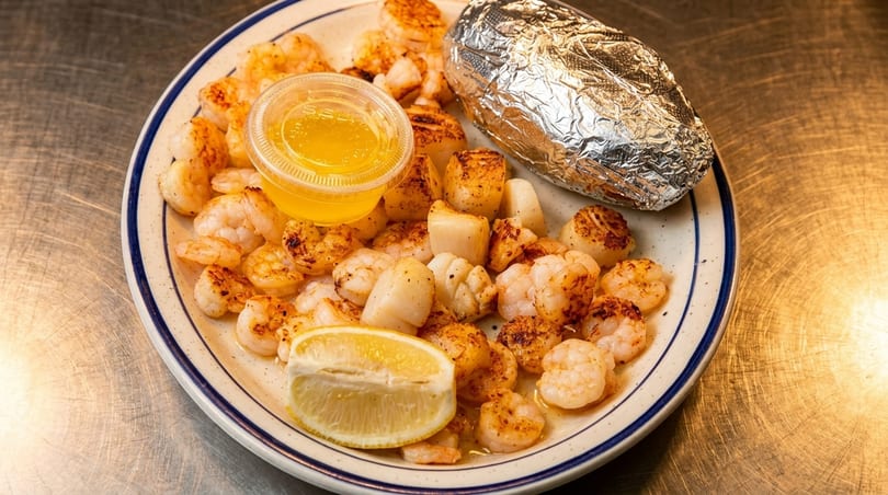 Grilled shrimp and scallops with a lemon wedge, melted butter, and a foil-wrapped baked potato.