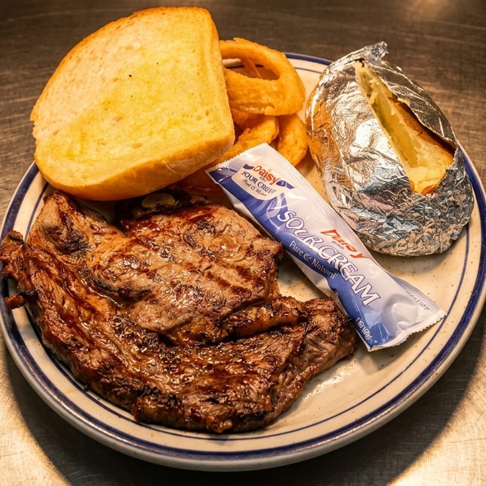 Grilled steak, baked potato, onion rings, garlic bread, and sour cream on a plate.