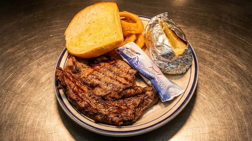 Grilled steak, baked potato, onion rings, garlic bread, and sour cream on a plate.